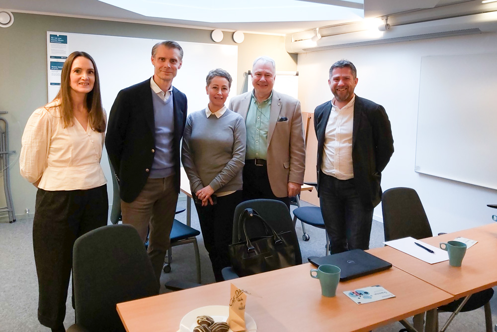 Leende besökare och presentatörer i ett konferensrum.